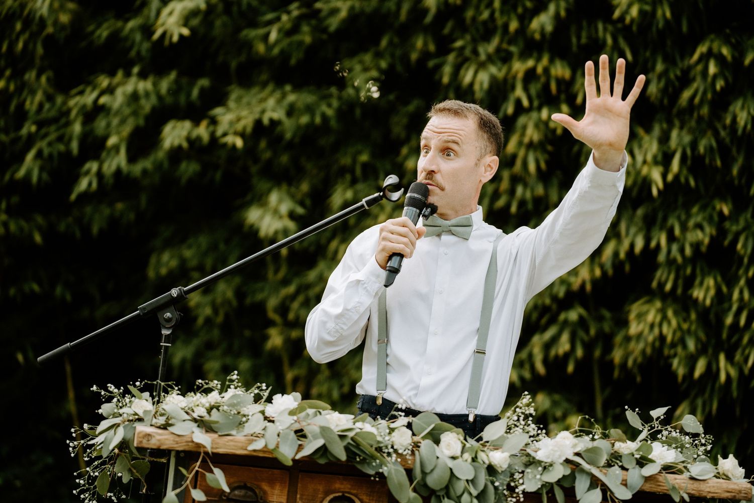 Wedding officiant speaking passionately at podium with raised hand outdoors.