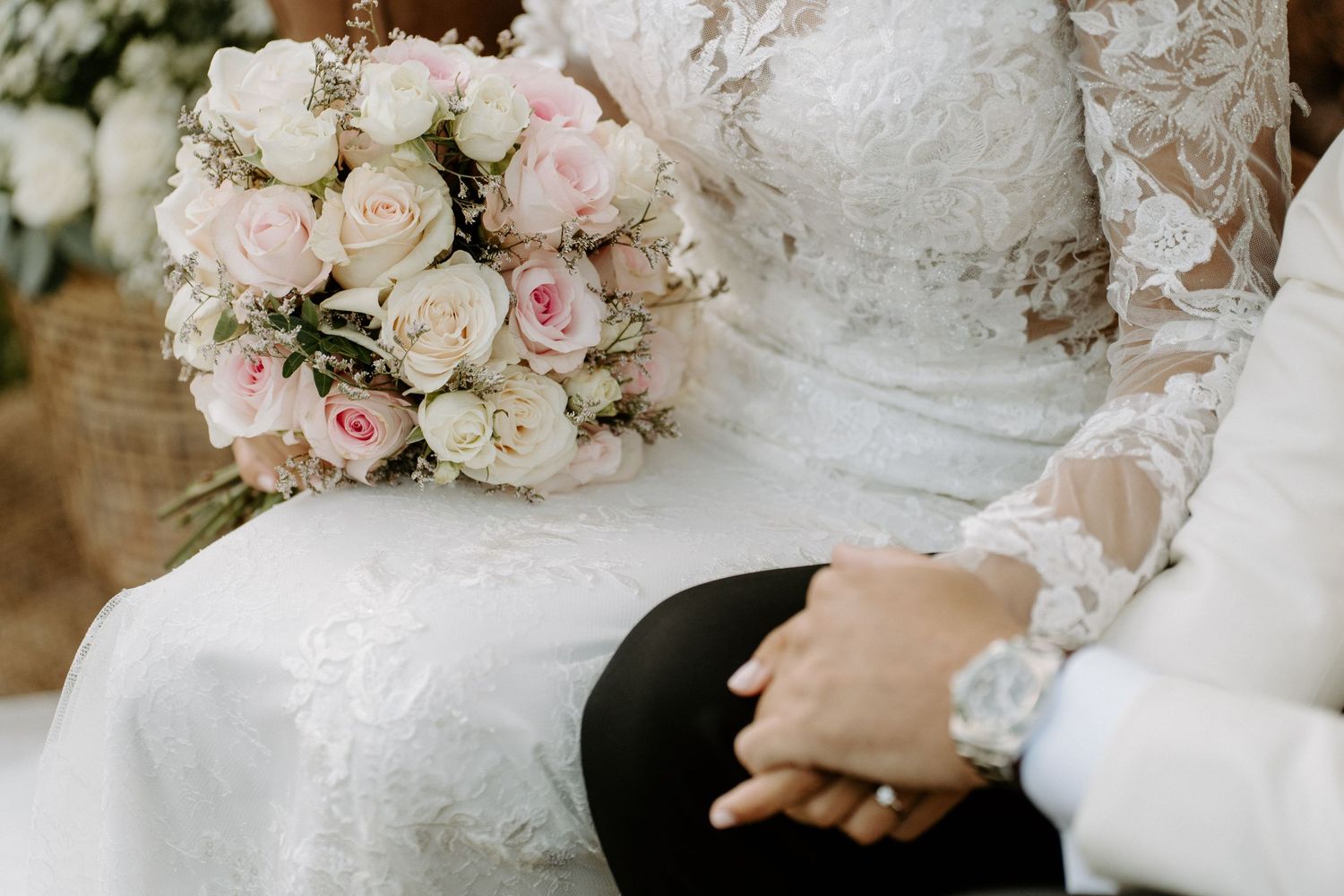 Bride in lace wedding dress holding a bouquet of pink and white roses with groom.