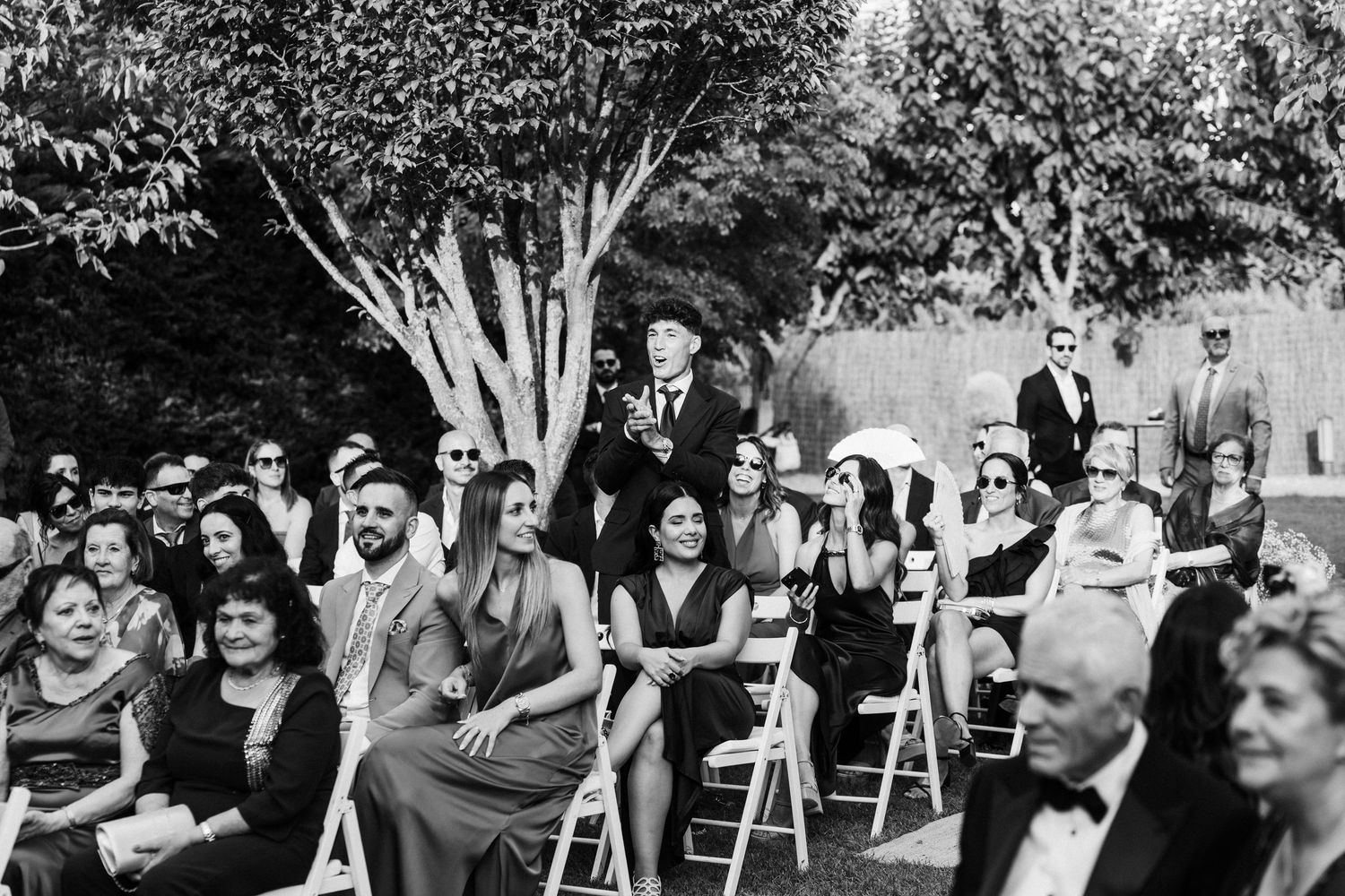 Wedding guests seated outdoors in garden ceremony, black and white photo capturing elegant crowd.