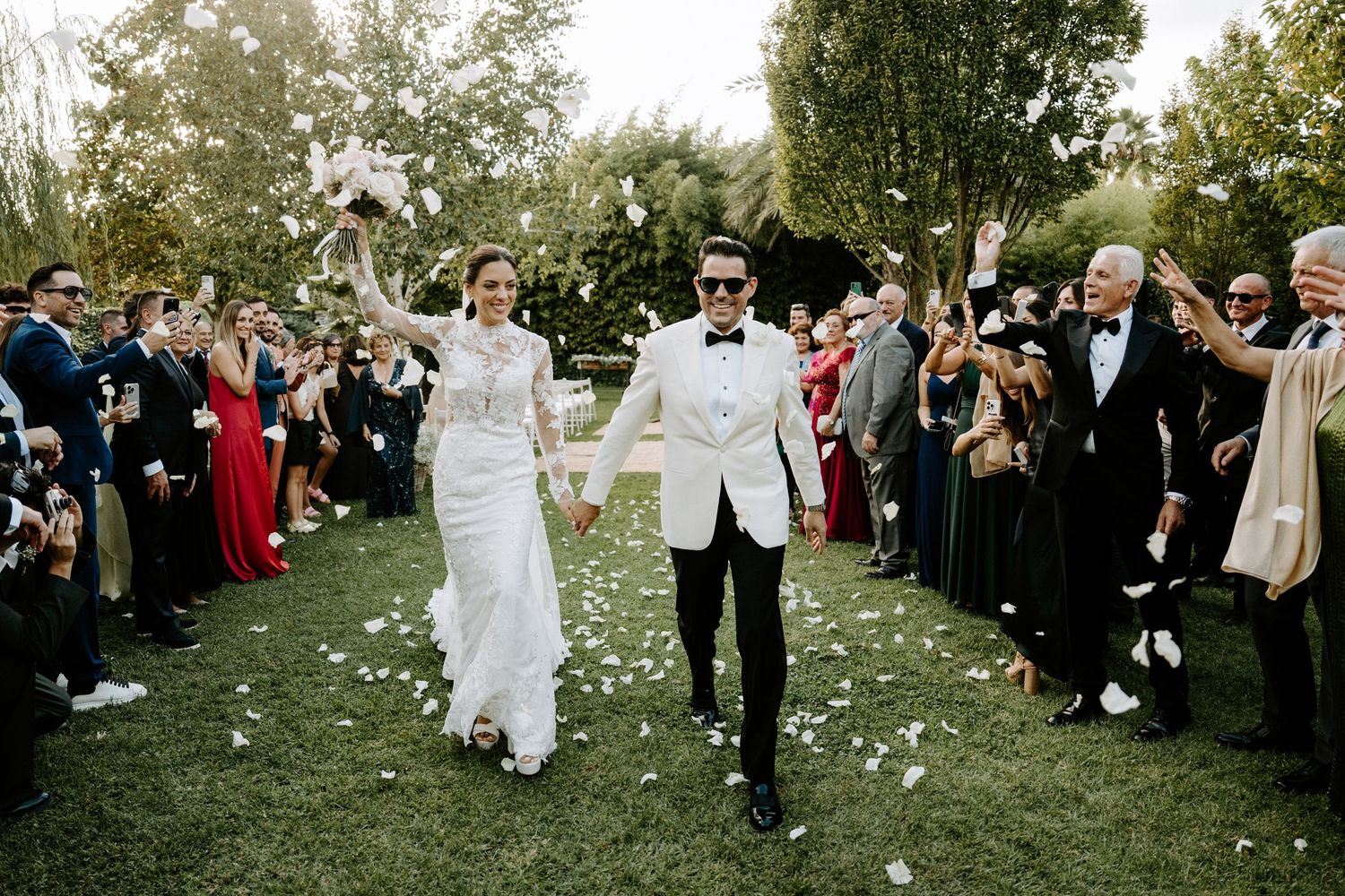 Bride and groom walking through confetti shower after outdoor wedding ceremony.