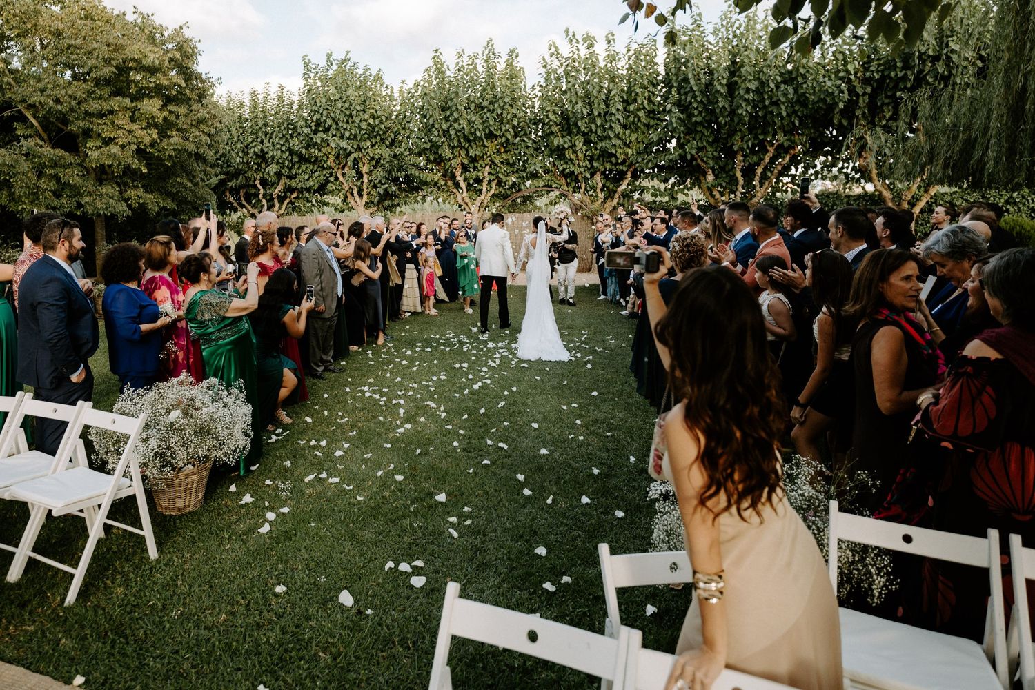 Aerial view of outdoor wedding ceremony with guests lining aisle as couple walks through garden venue.