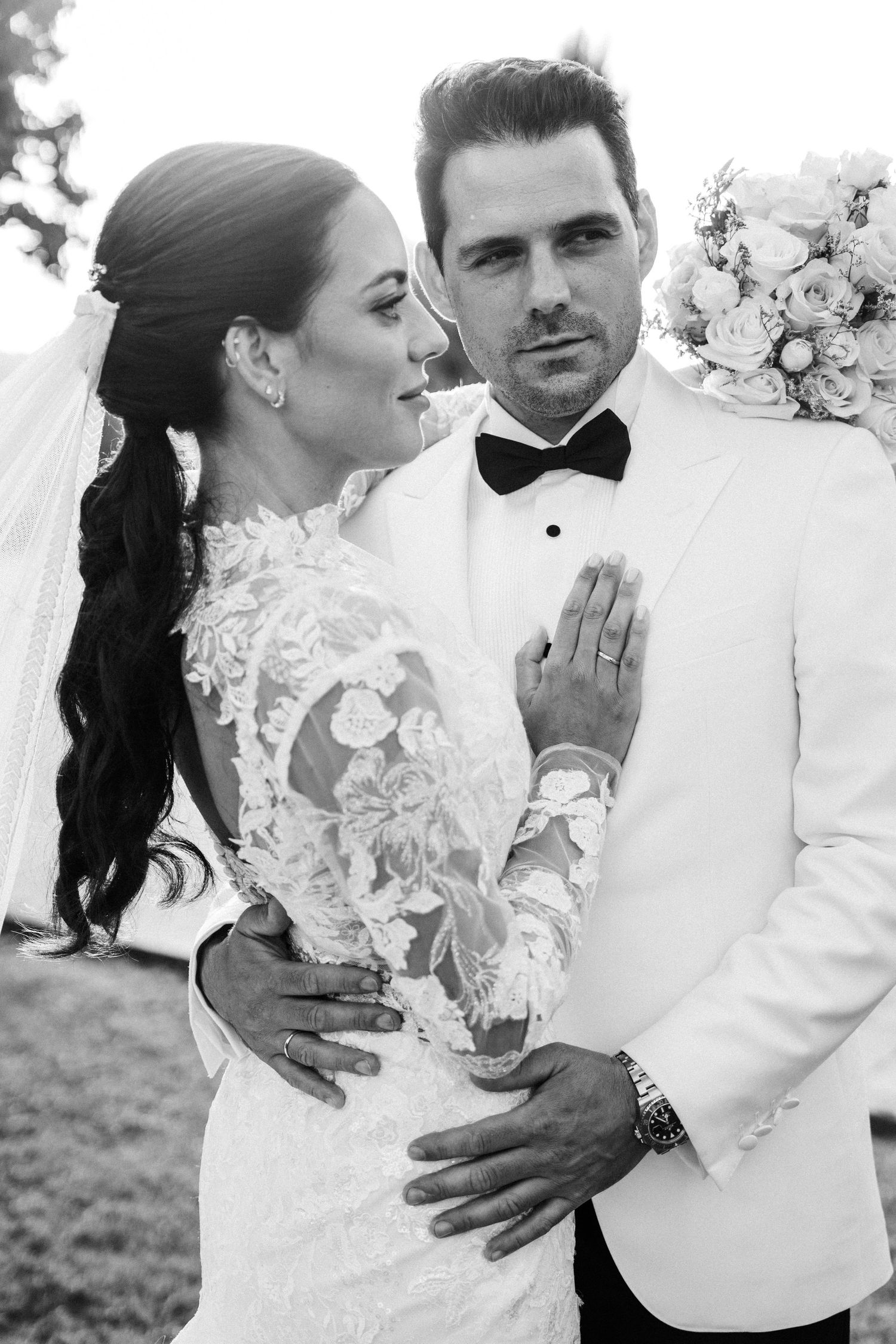 Elegant bride and groom pose together in black and white wedding portrait, she in lace gown, he in white tuxedo.