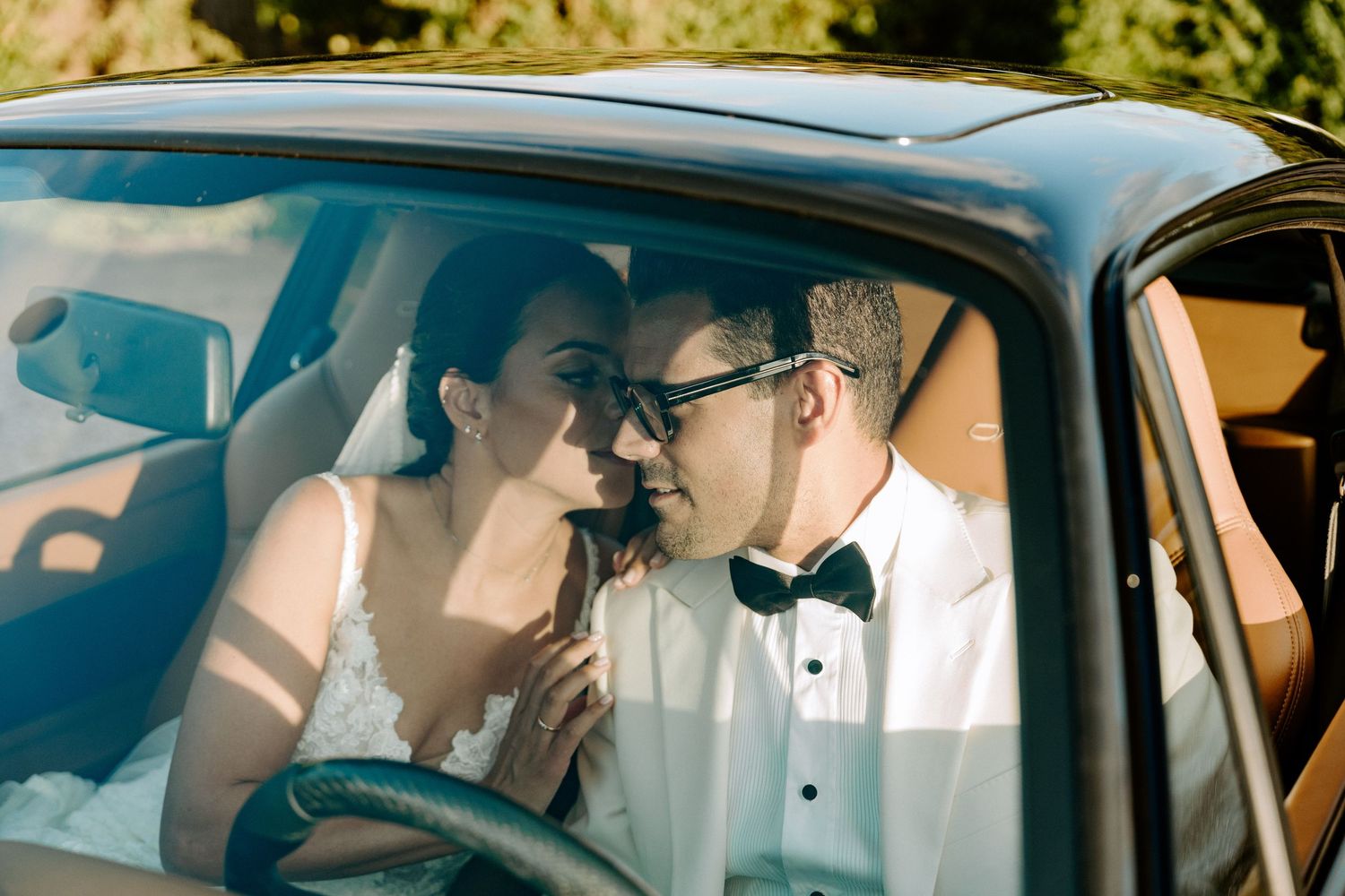 Bride and groom sharing intimate moment inside vintage classic wedding car.