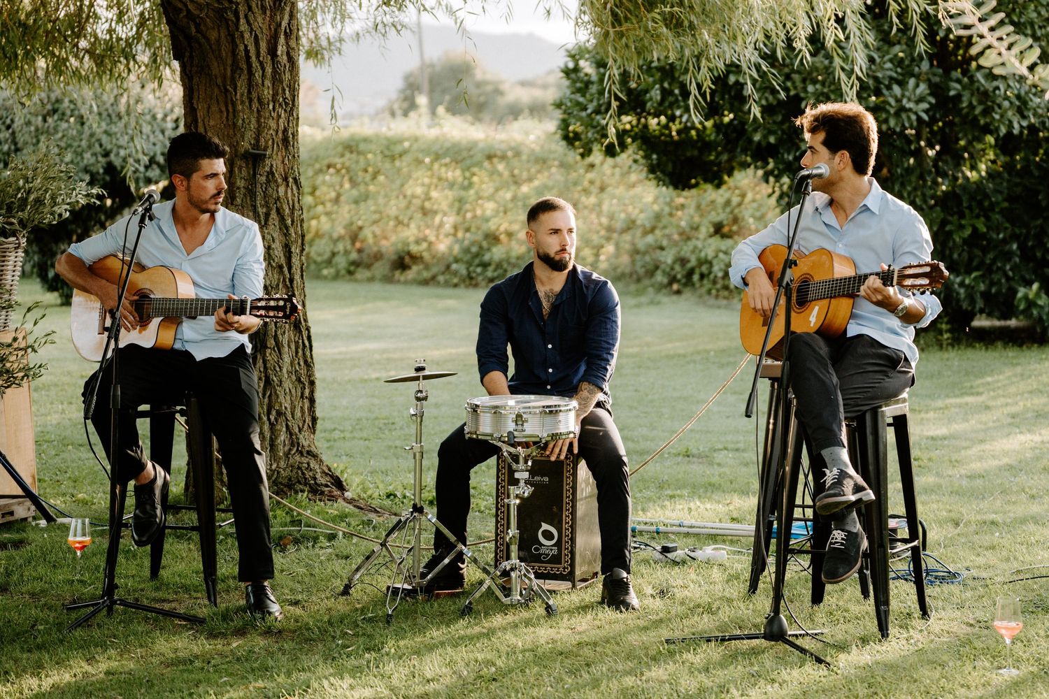 Trio of musicians perform with guitars and drums at outdoor wedding reception.