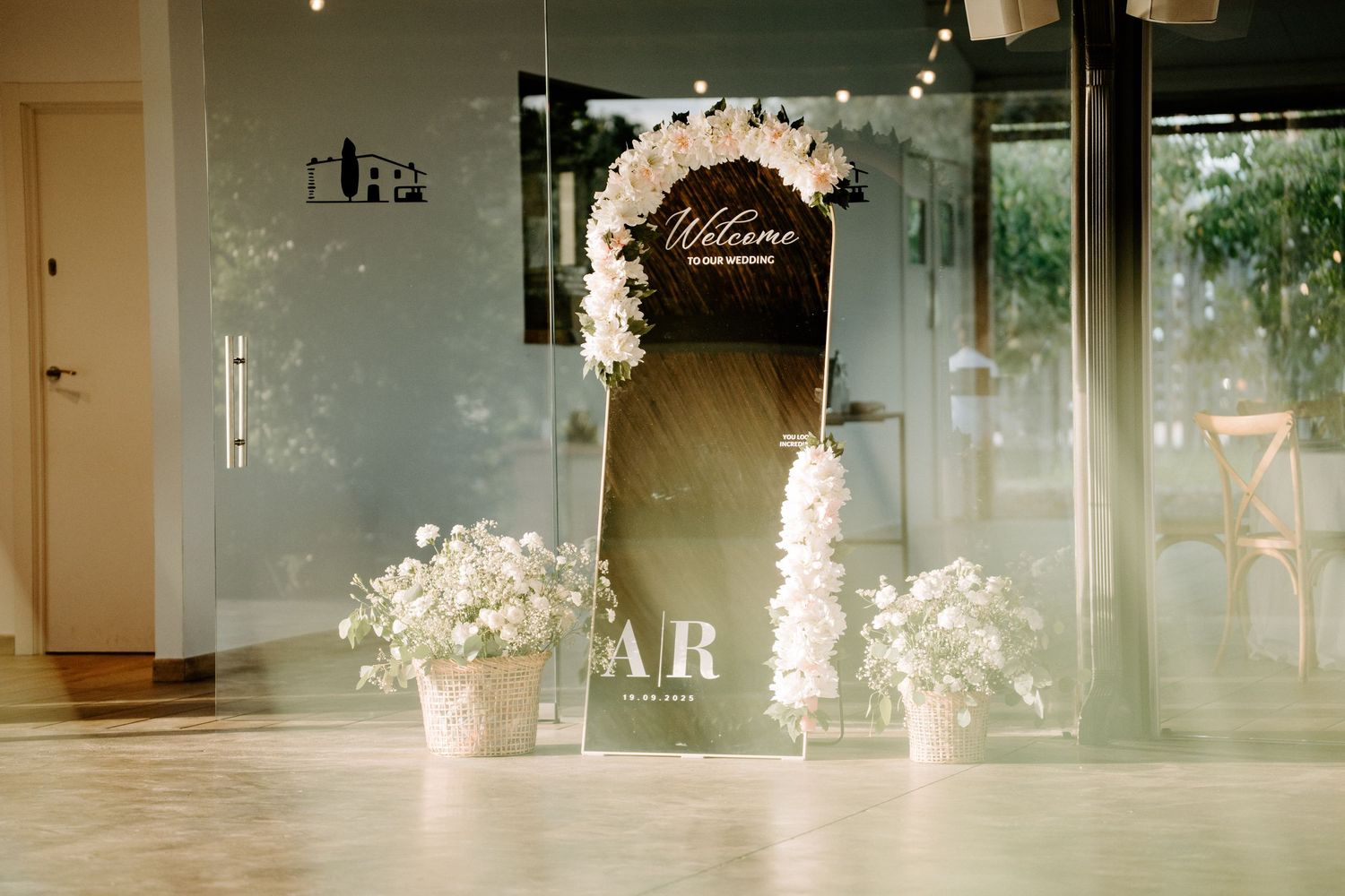 Elegant wedding welcome sign with floral arch and white flower arrangements at venue entrance.