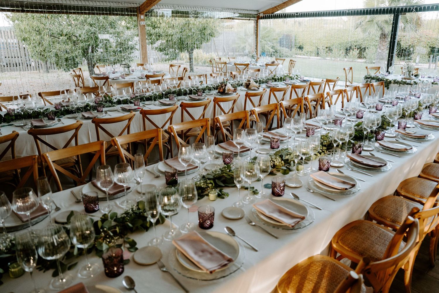 Elegantly set long reception tables with greenery and glassware for wedding.