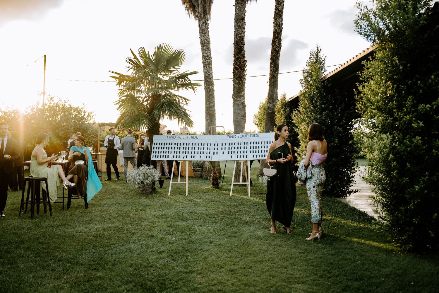 Outdoor wedding cocktail hour with guests mingling near seating chart displays at golden sunset.