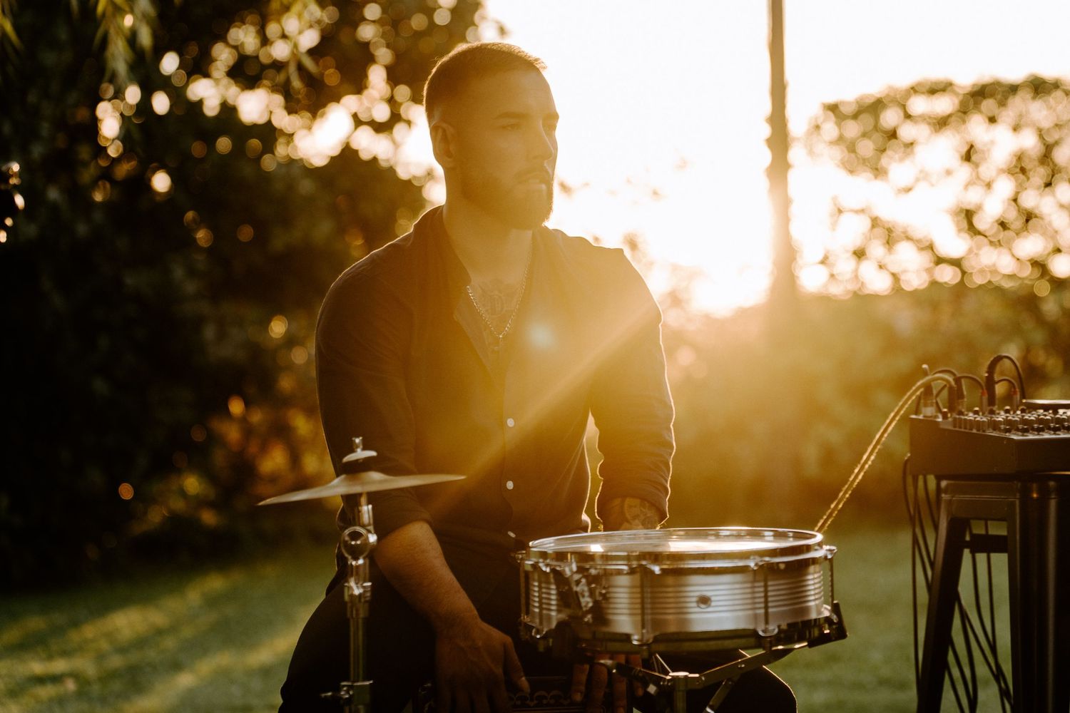 Drummer performing at golden hour sunset during outdoor wedding reception with warm glowing light.