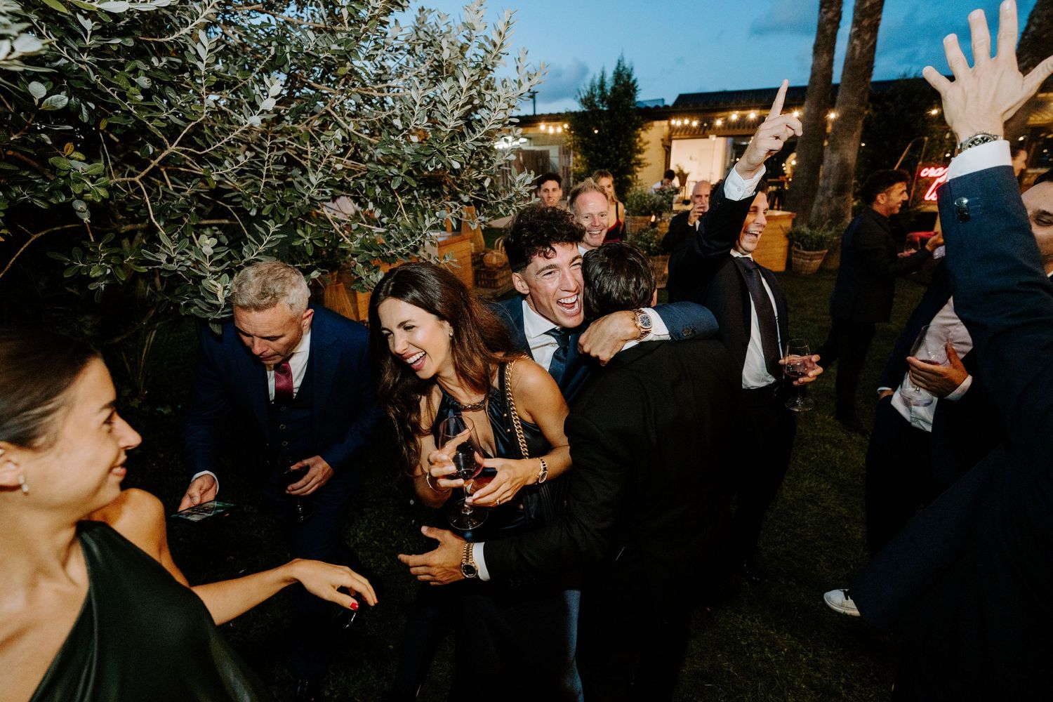 Wedding guests laughing and celebrating together outdoors during evening reception party.