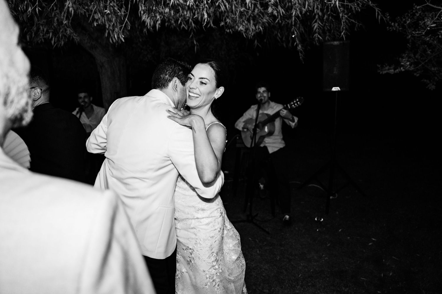 Black and white photo of bride and groom sharing first dance with live guitarist performing nearby.