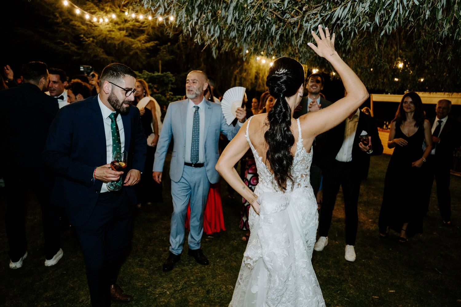 Bride in lace wedding gown dances outdoors at night wedding reception with guests.