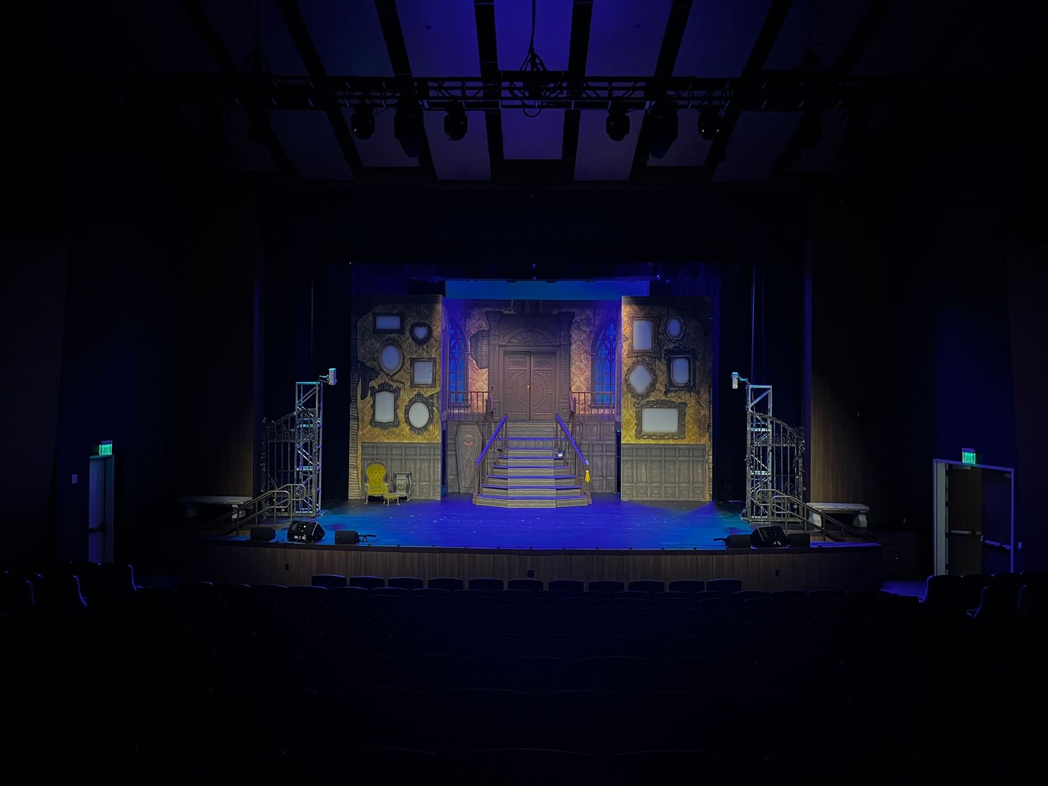 Empty theater stage with blue lighting illuminates an ornate set featuring frames and a grand staircase.