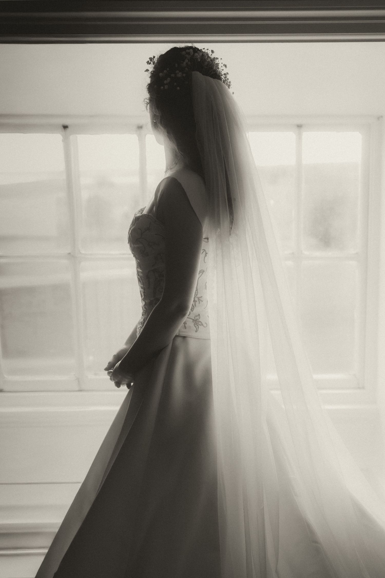 A silhouette of a bride in a flowing wedding dress and veil, standing in a window frame.