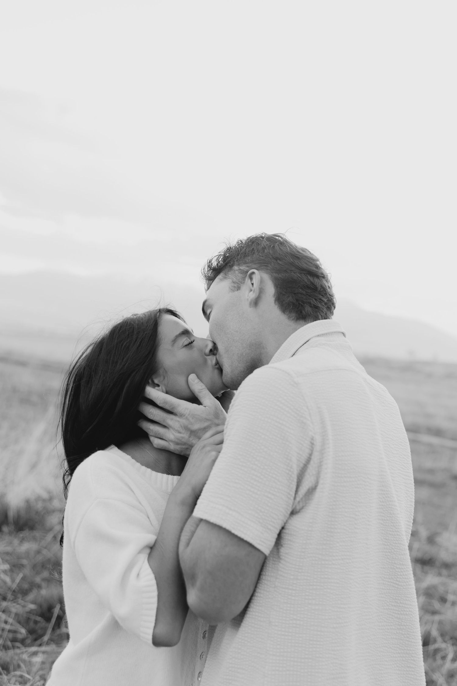 A romantic couple sharing an intimate kiss in a black and white photo series.