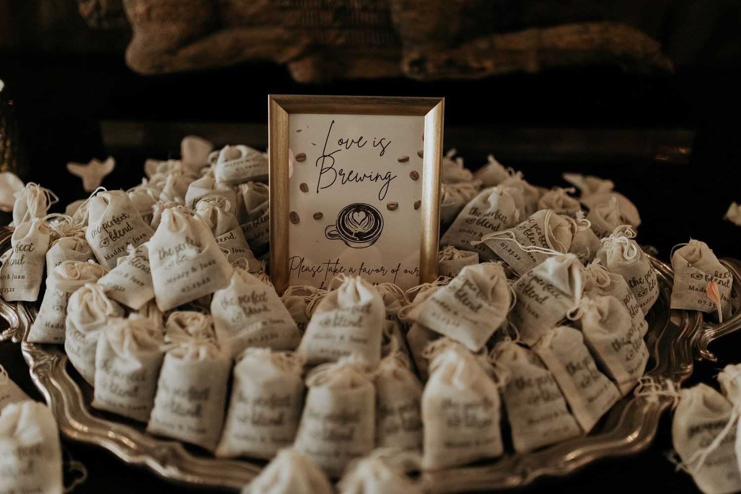 Wedding favor display with burlap bags and a gold-framed Love is Brewing sign on a silver tray.