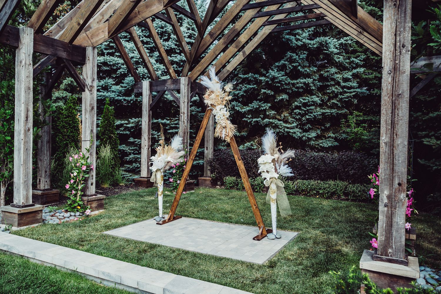 Outdoor wedding ceremony arch with white floral arrangements under a wooden pergola surrounded by lush greenery.