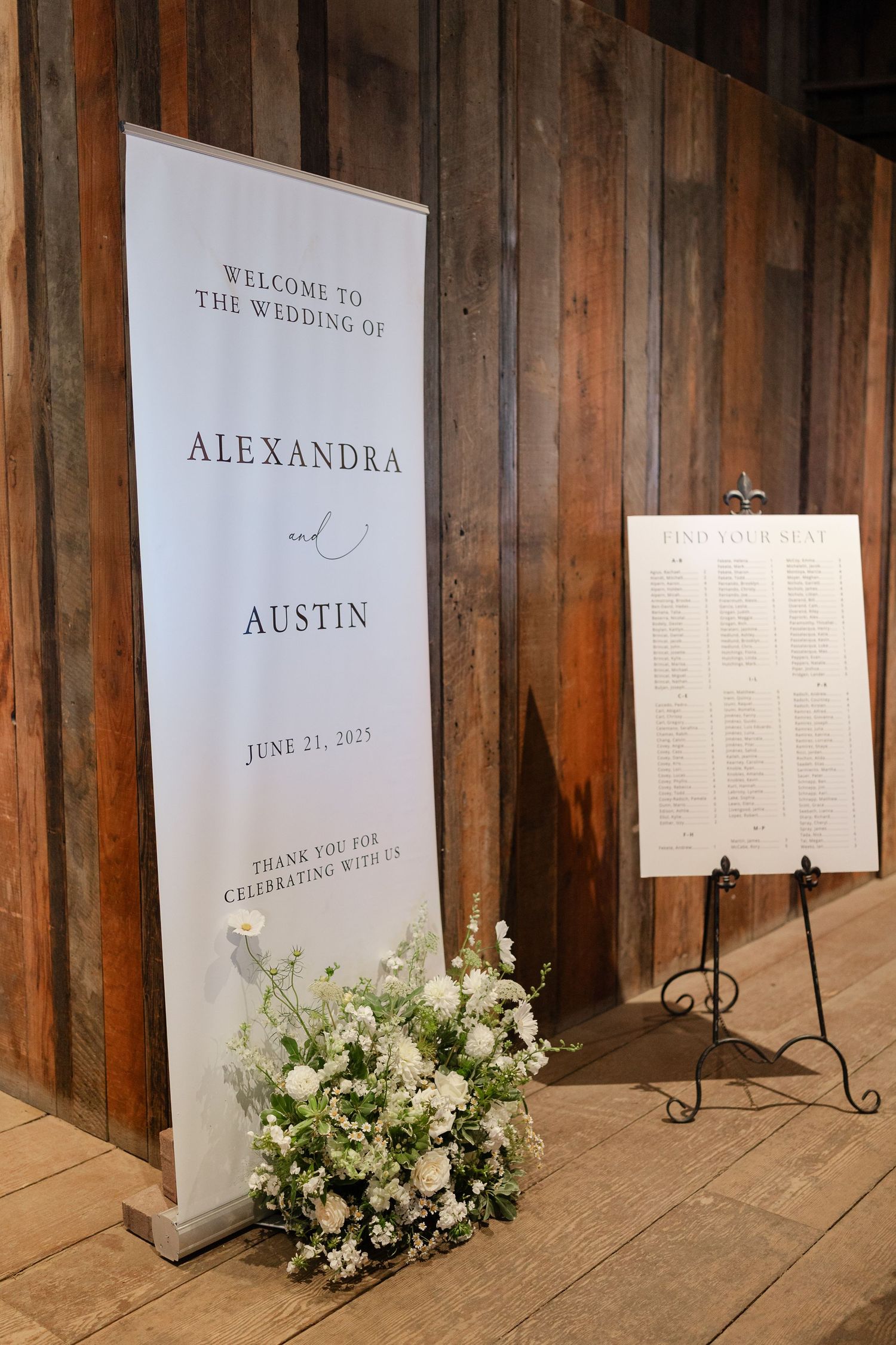 Wedding welcome signs and seating charts displayed against rustic wooden barn walls with white floral arrangements.