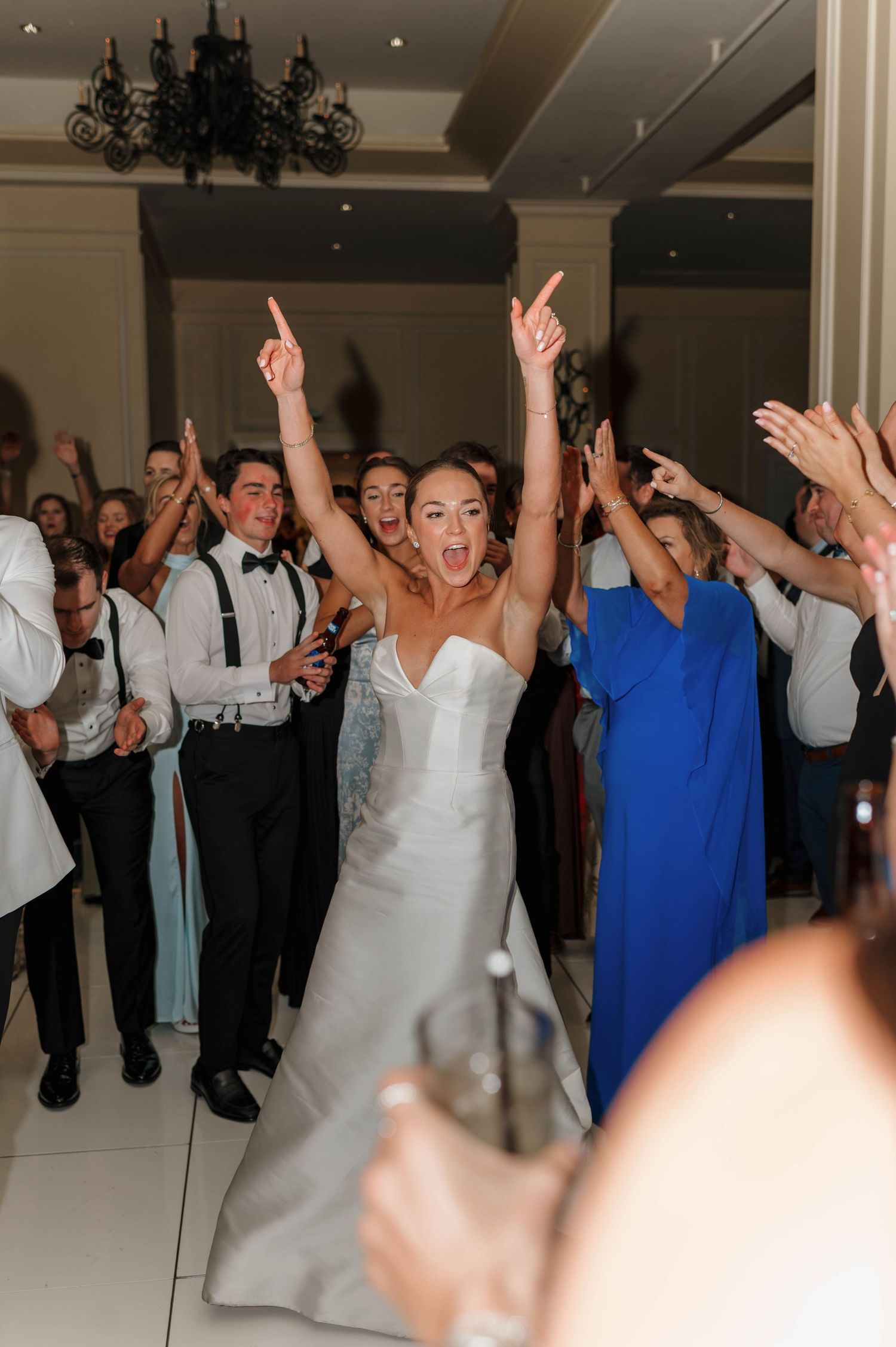 Wedding guests and newlyweds dance with raised arms and joyful expressions during a lively reception celebration.