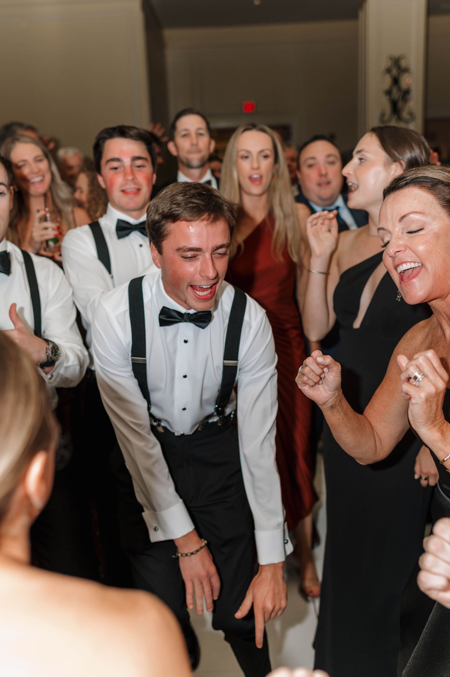 A lively group of wedding guests in formal attire dancing and laughing together at a reception.