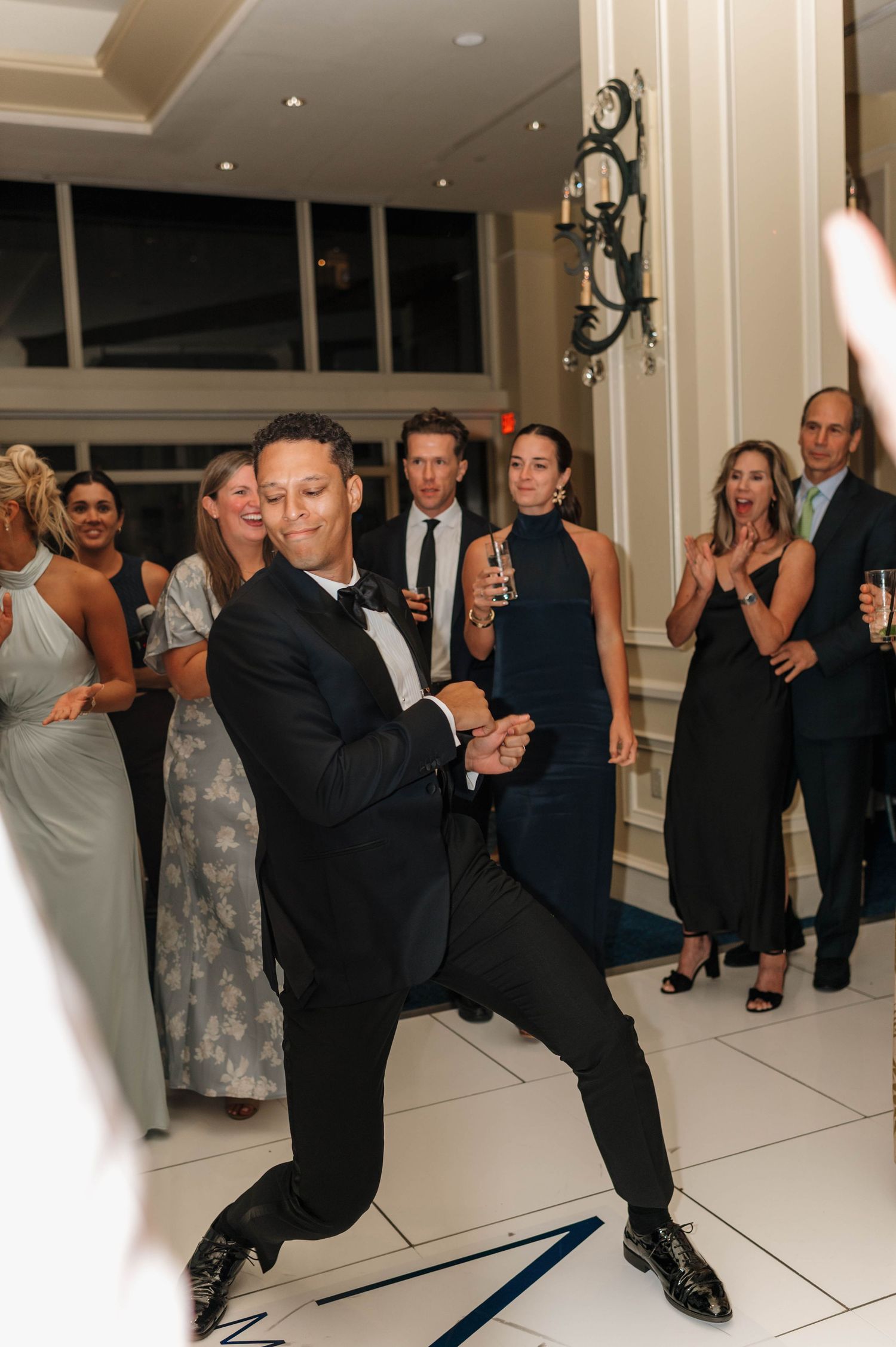 Wedding guests perform synchronized dance moves on a white dance floor during a reception celebration.