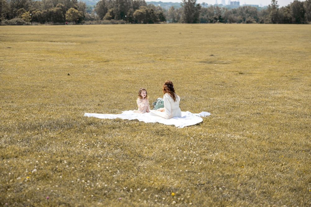 Two people having an outdoor picnic on a white blanket in a vast golden field on a sunny day.