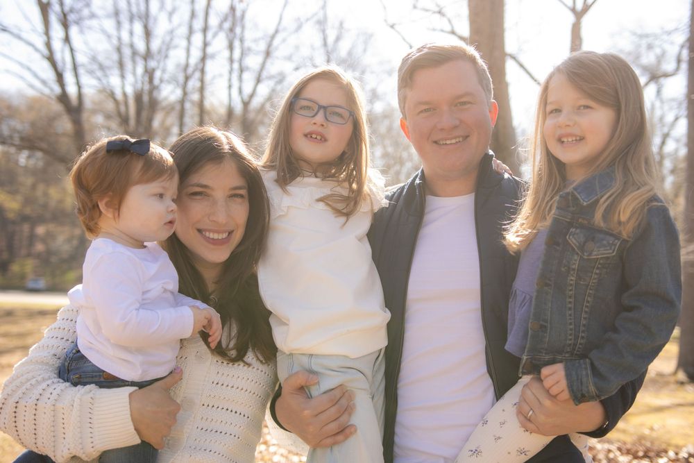 A family group poses together outdoors on a sunny autumn day in a park setting.