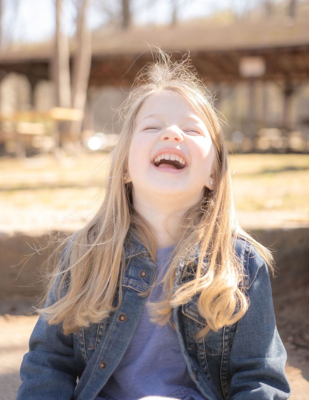 A child with blonde hair laughs with pure joy outdoors on a sunny autumn day.