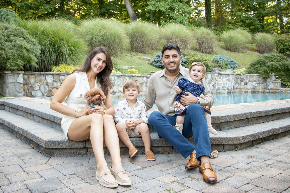Group sits on stone steps together outdoors with ornamental grasses and stone wall in background.
