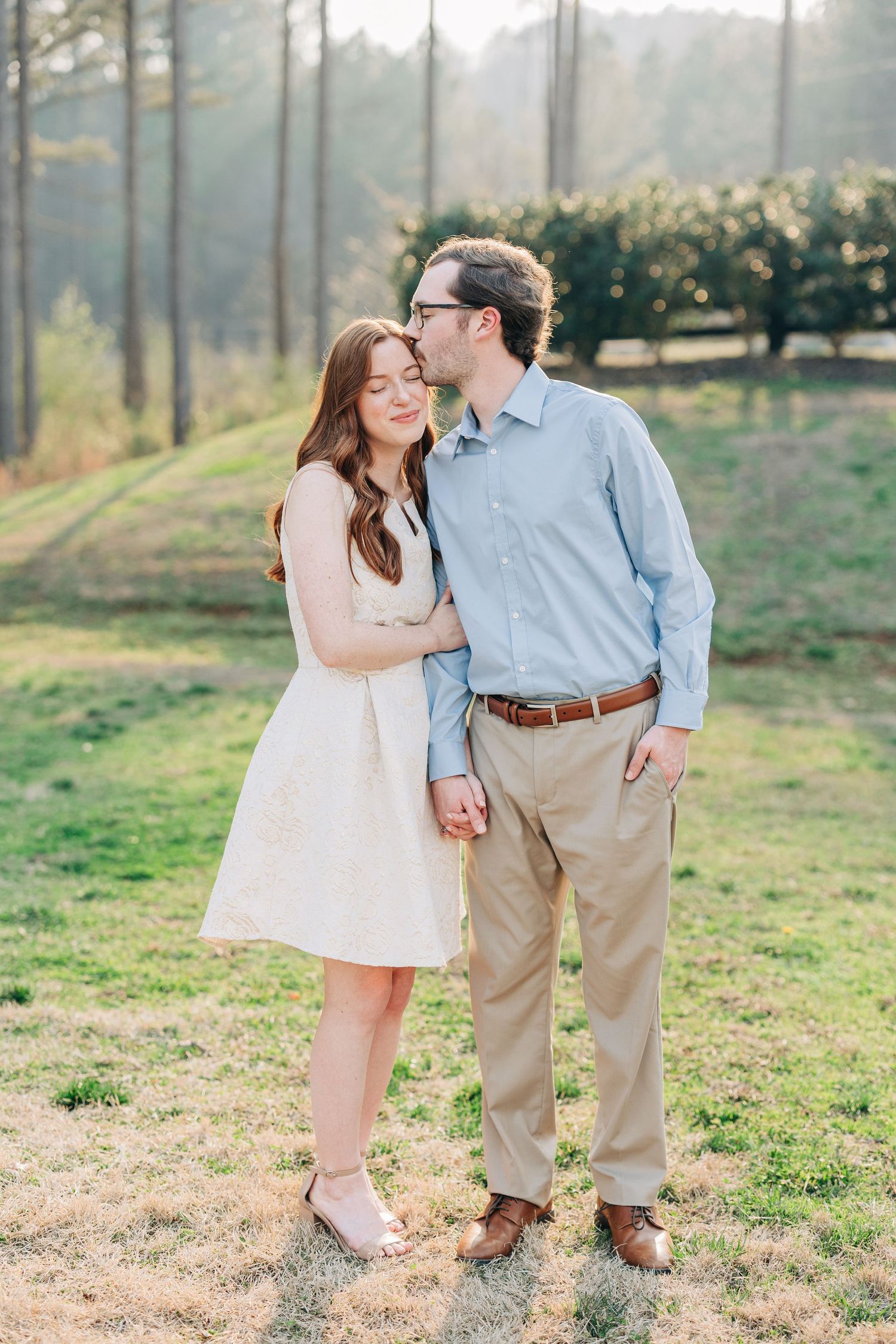 A romantic couple shares tender moments in a sunny meadow wearing coordinated light casual outfits.