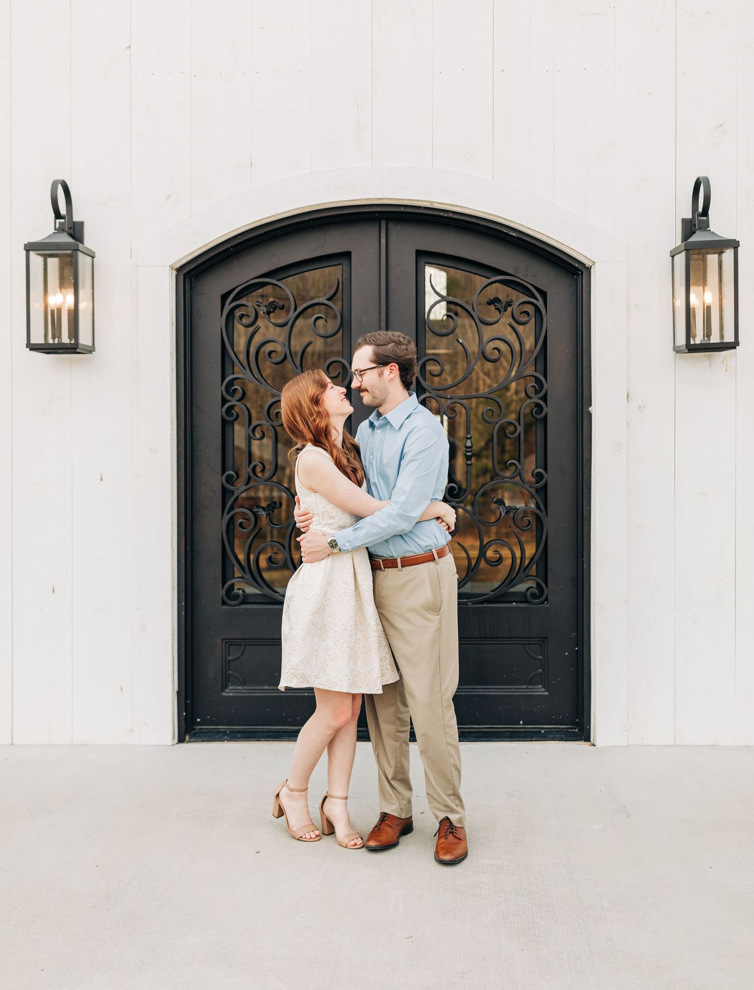 Couple shares romantic moments in front of elegant black iron doors on white building exterior.