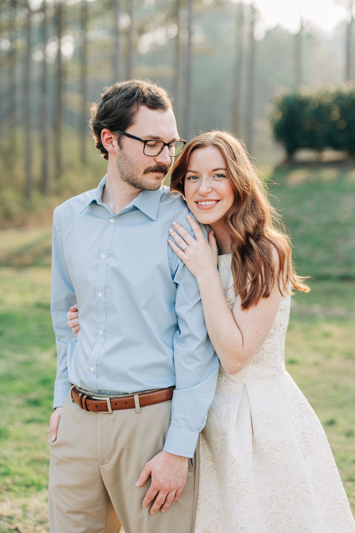 A couple shares intimate moments in a grassy field while wearing coordinated blue and white outfits during their engagement session.