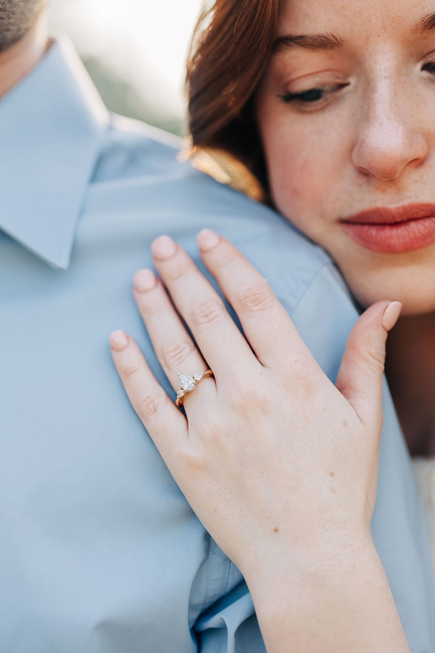 Close-up photo of an engagement ring on a hand with soft blue fabric background.