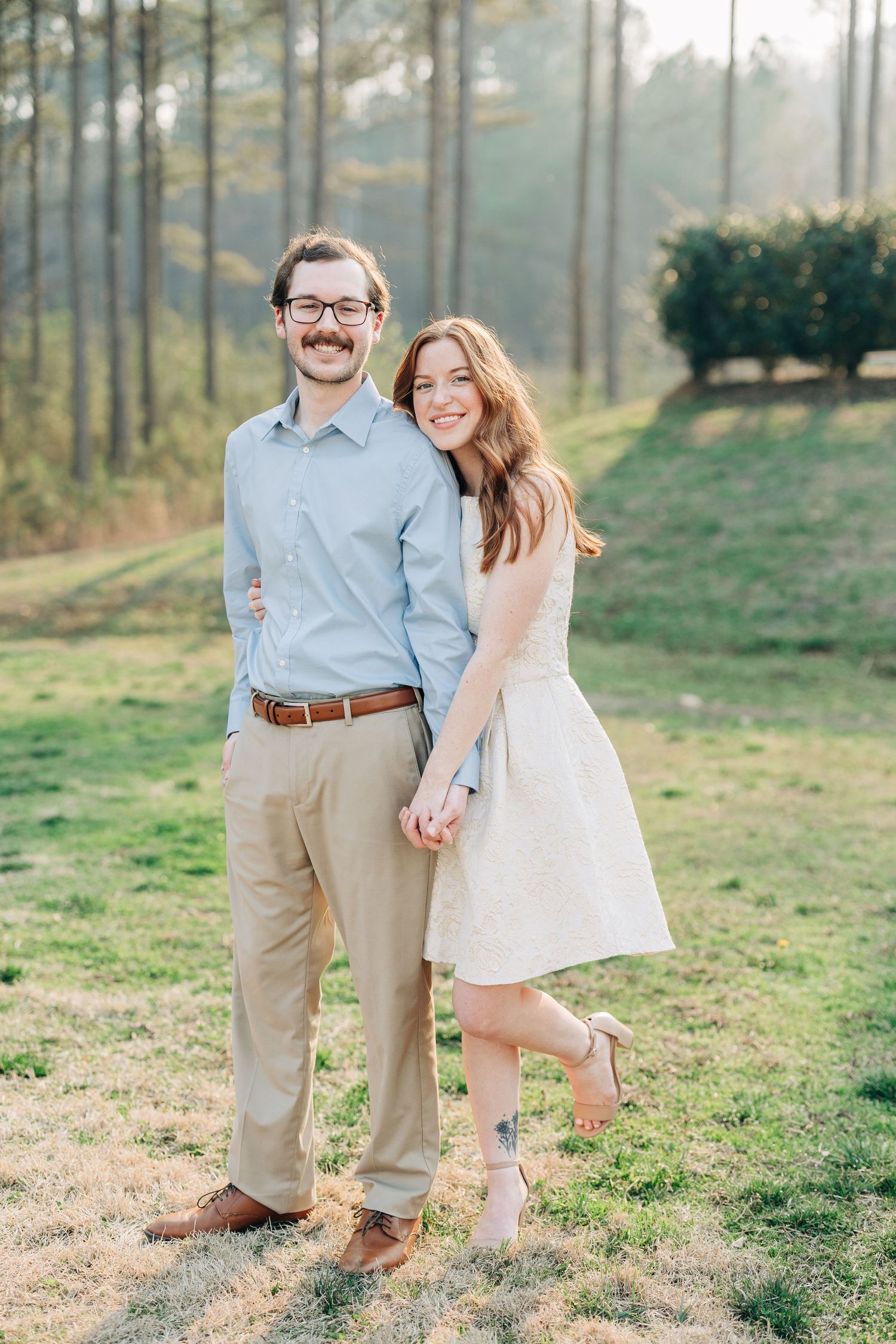A romantic outdoor photo session in a grassy field with pine trees in the background at golden hour.