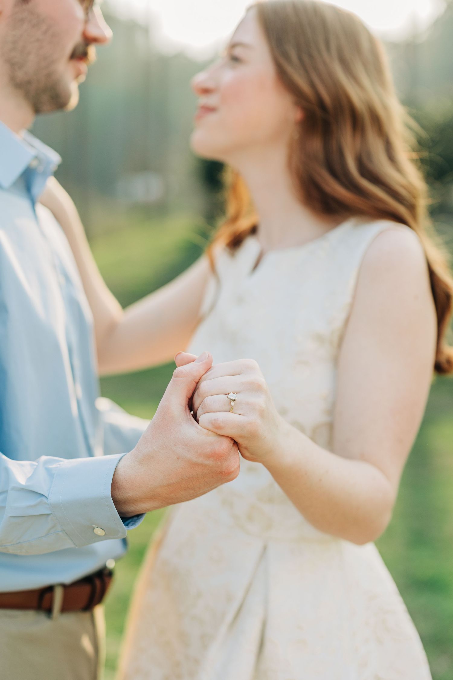 A couple in light colored clothing hold hands and dance together in a romantic outdoor setting during golden hour.