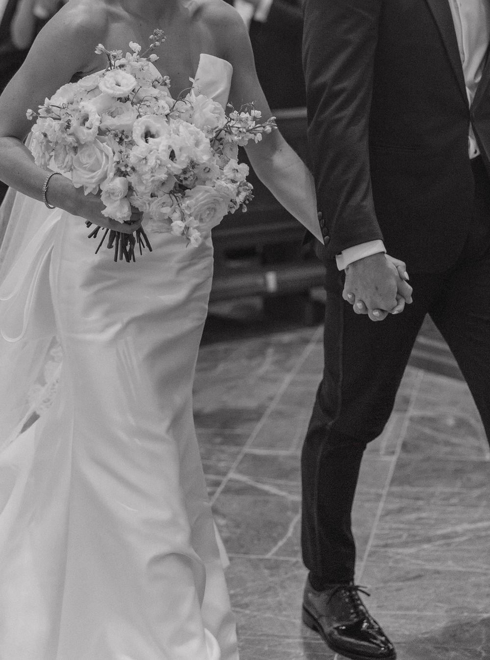 Black and white wedding photo showing dress details and formal footwear of a bride and groom on a tiled floor.