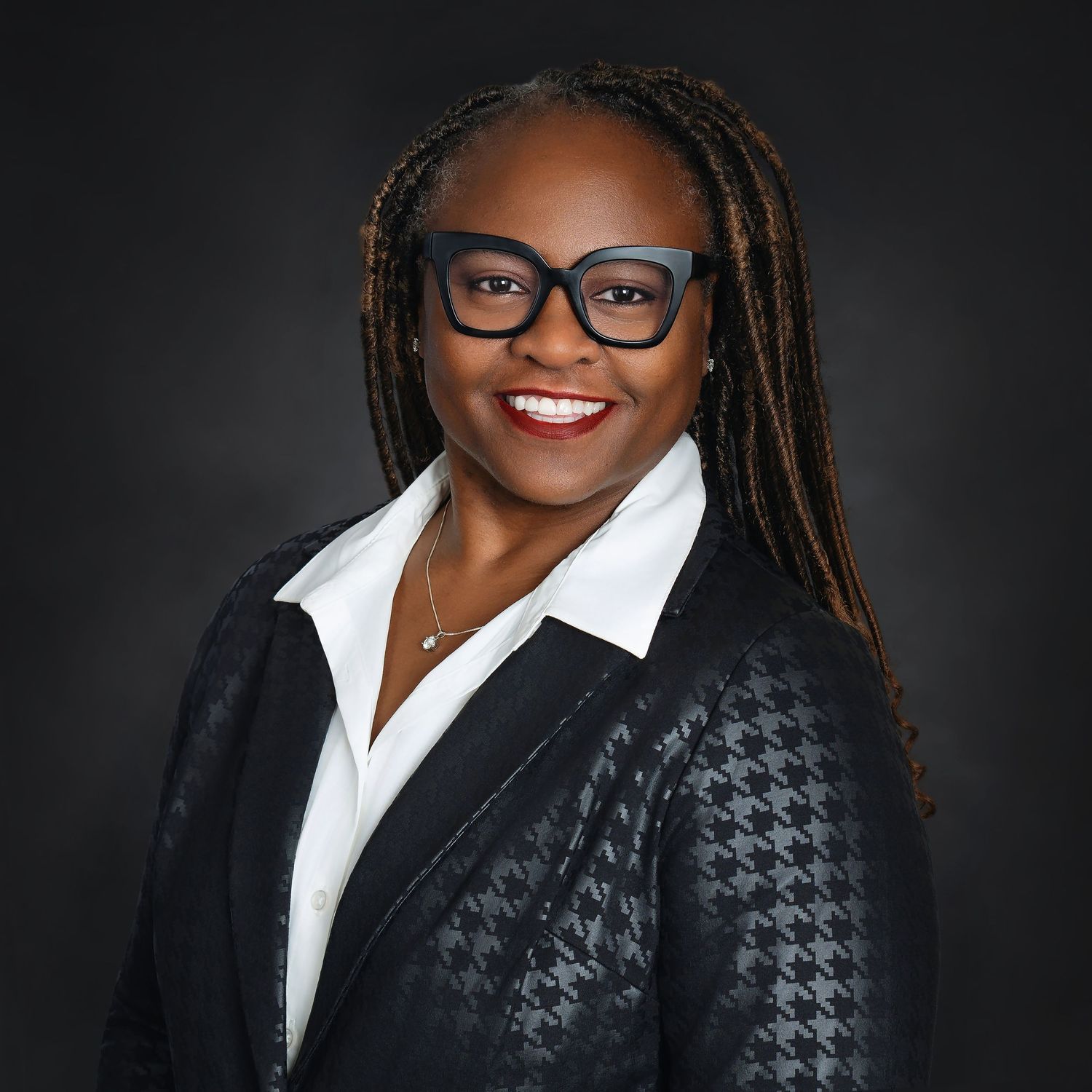 Professional headshot of a businessperson wearing glasses, a black houndstooth blazer and white collared shirt.