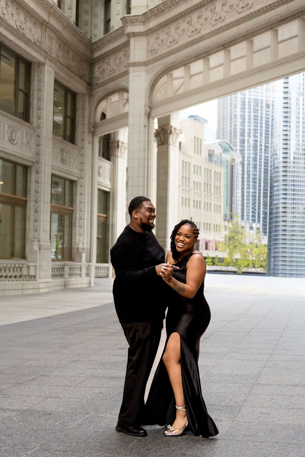 Couple dancing joyfully in black formal wear outside a grand Chicago architectural building.