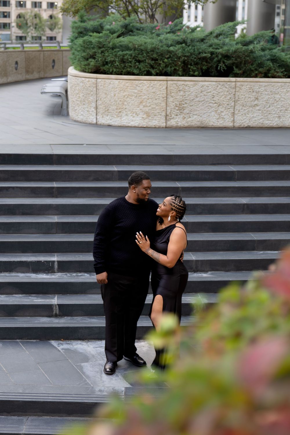 Couple sharing a romantic moment on urban stone steps surrounded by lush greenery.