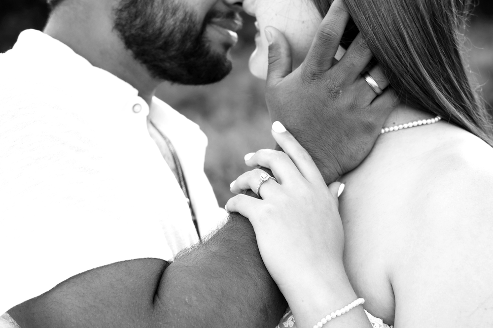 Black and white close-up of an engaged couple sharing a tender moment, showcasing a diamond engagement ring.
