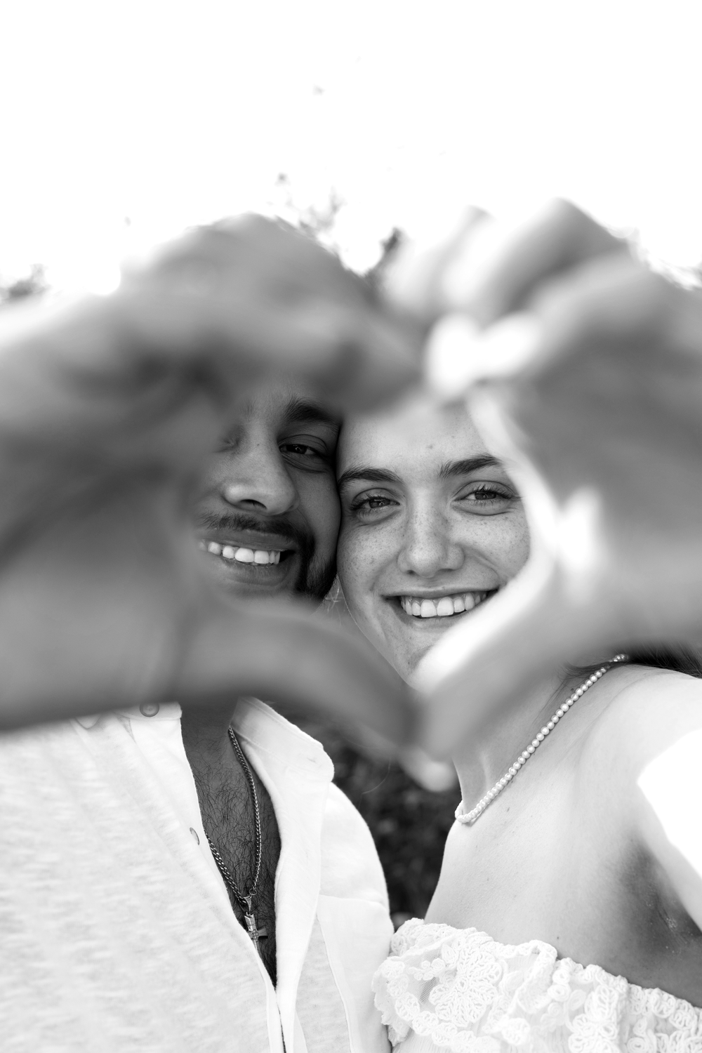 Smiling couple making a heart shape with their hands in a romantic black and white engagement photo.