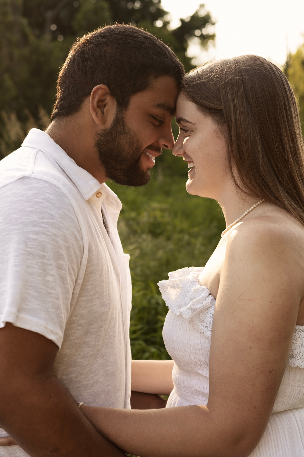 Romantic couple touching foreheads and smiling face-to-face in a warm golden hour outdoor portrait.