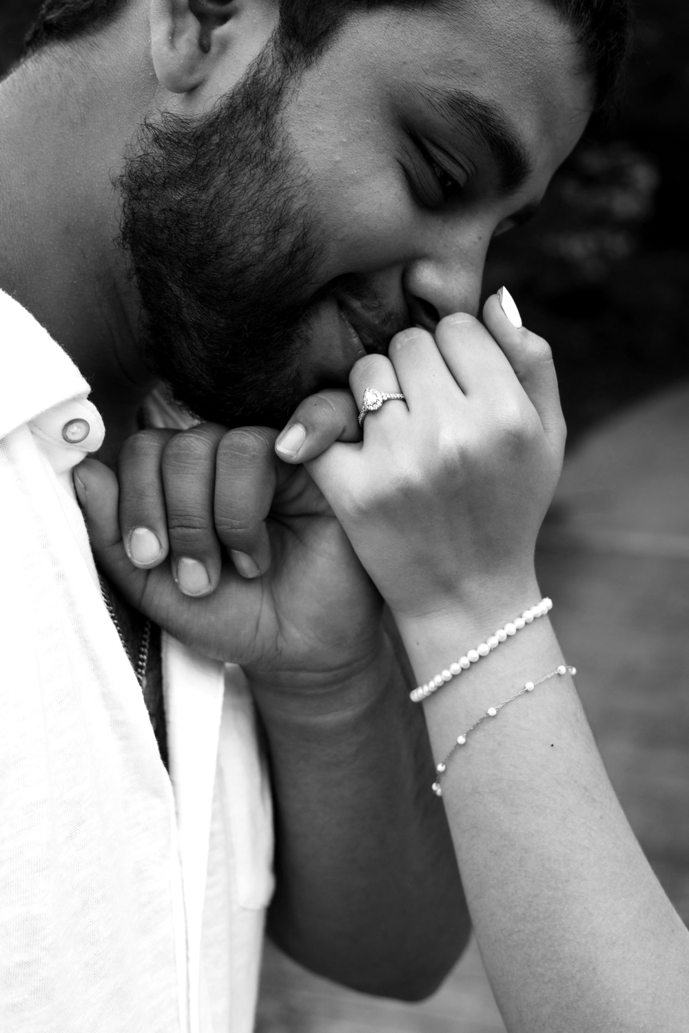 Black and white romantic photo of a bearded man kissing his partner's hand adorned with an engagement ring.