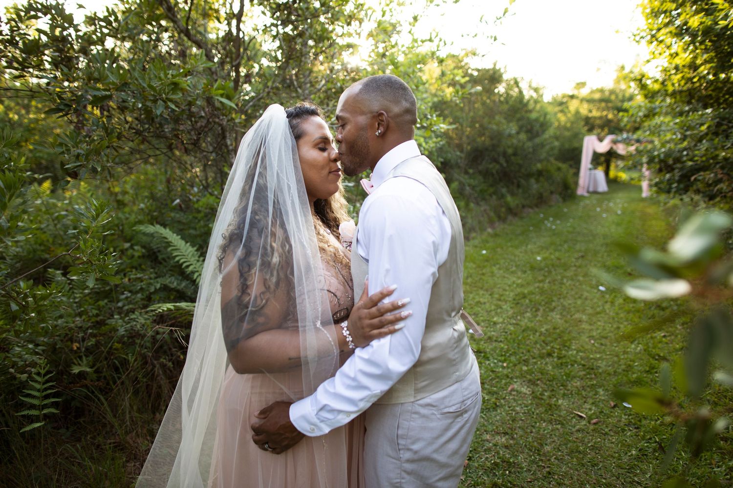 A couple shares a romantic kiss in a sunlit garden setting during their wedding ceremony.