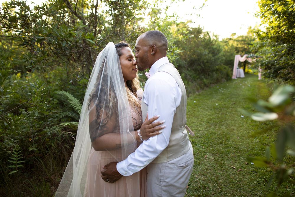 A couple shares a romantic kiss in a sunlit garden setting during their wedding ceremony.