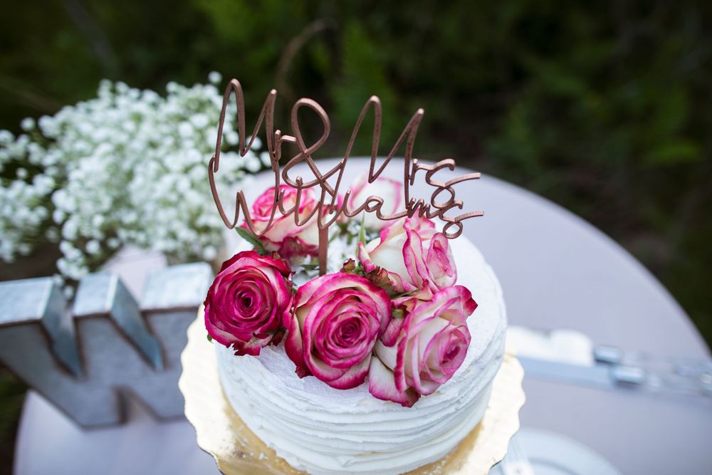 A collection of elegant pink rose-topped wedding cakes displayed outdoors with delicate floral decorations.
