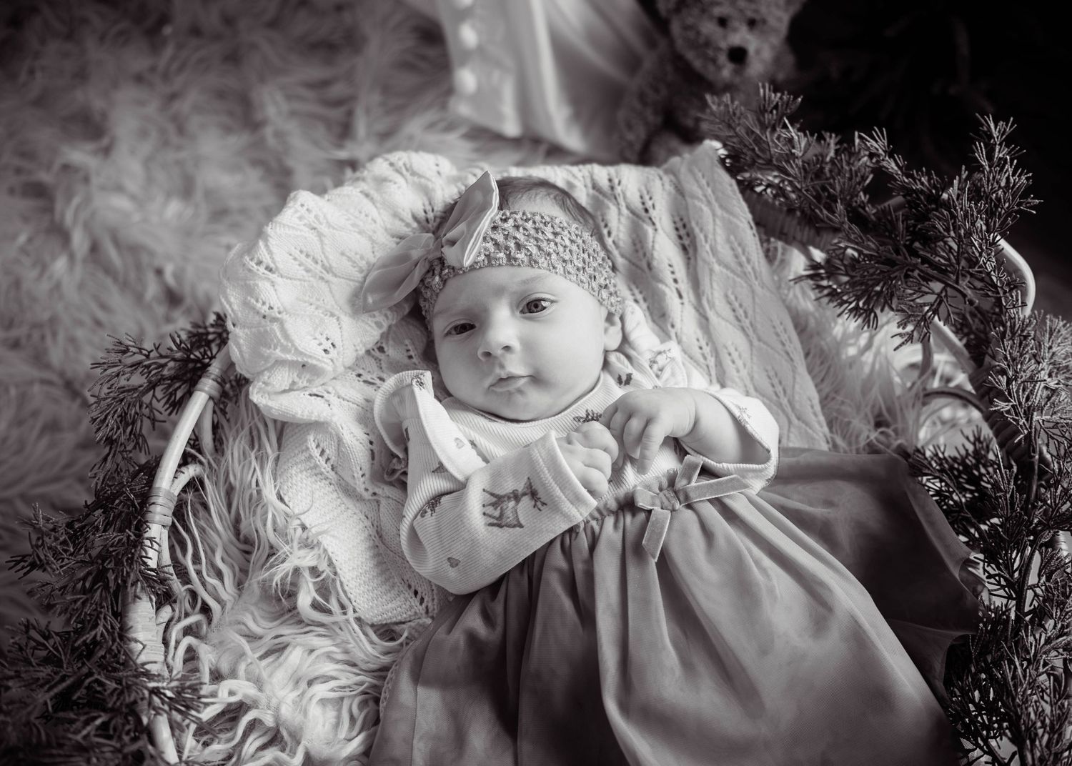 Adorable newborn baby in a white outfit lying in a basket with Christmas decorations in black and white.