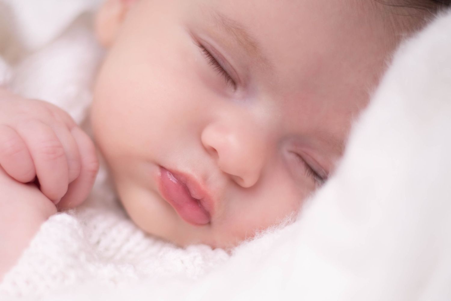 Peaceful newborn baby sleeping soundly wrapped in soft white blanket. Newborn photography in Blackwood South Wales