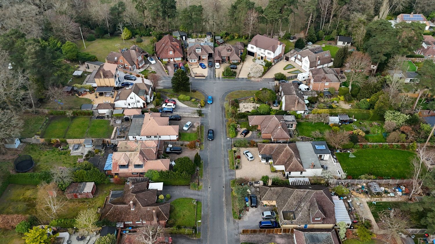Aerial panoramic view of a suburban neighborhood with houses and streets surrounded by trees and greenery.