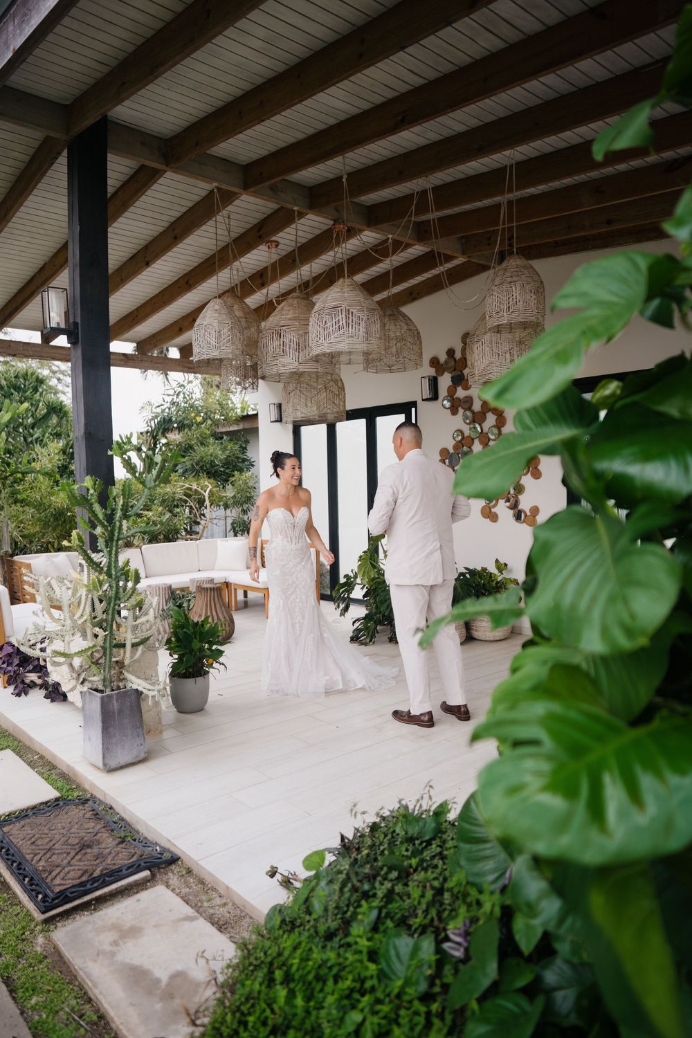 A covered outdoor patio decorated with woven pendant lights and tropical plants creates an elegant wedding venue setting.