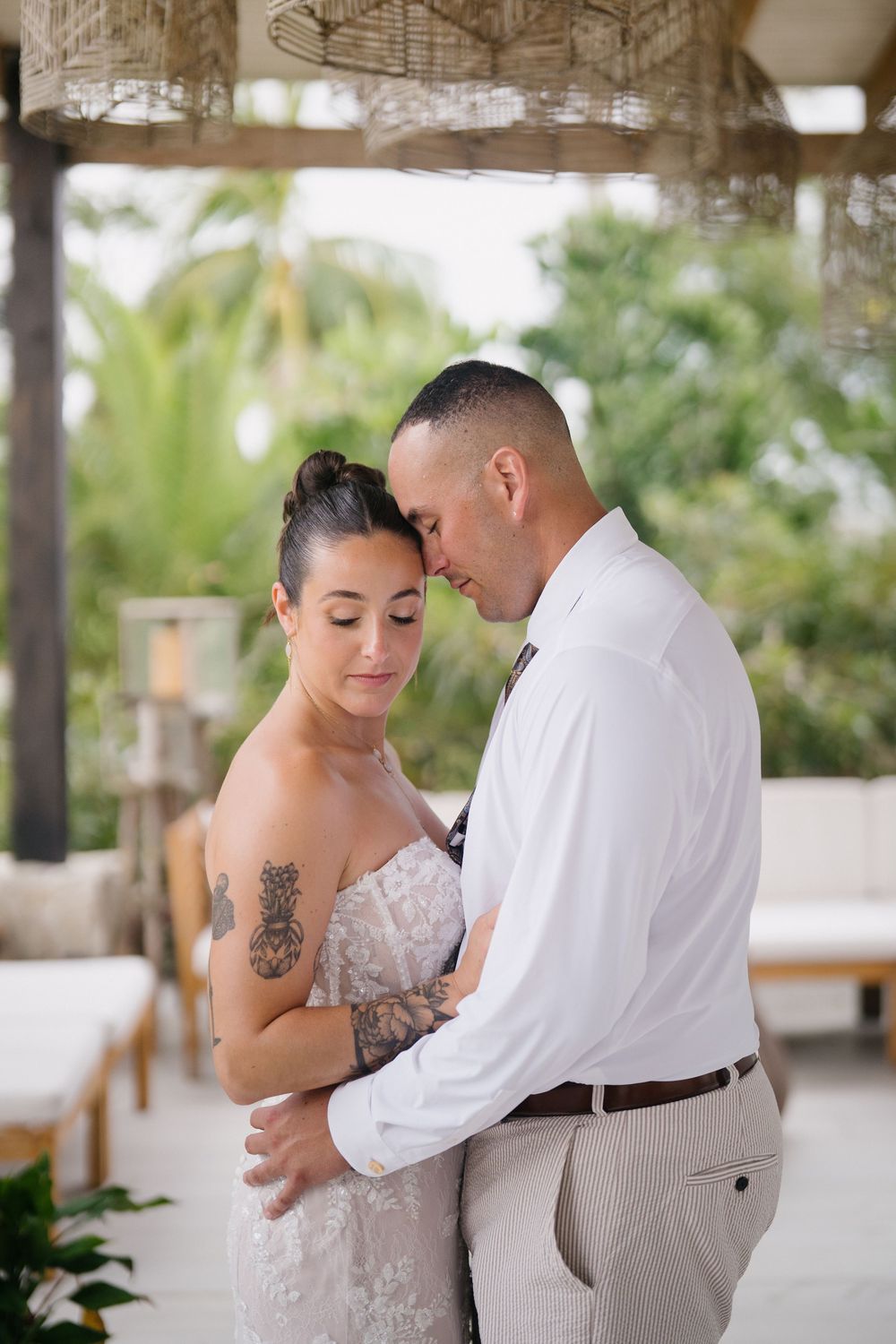 Romantic wedding couple shares an intimate dance moment on a covered outdoor patio surrounded by tropical greenery.
